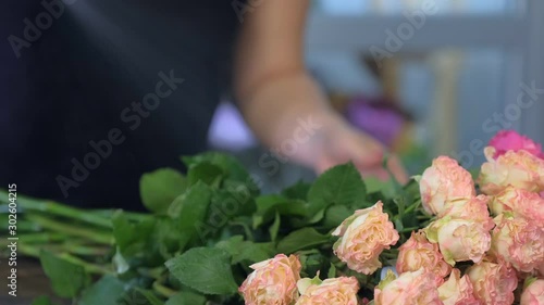 Florist woman making bouquet of pink peonies in flower shop, closeup view. Floral business concept. She creates professional bunch composition in floristic studio store, spraying flowers water.