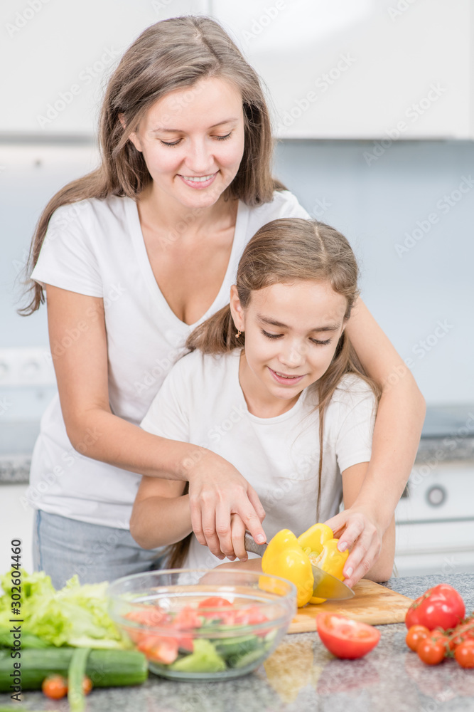 Happy family at home. Mom teaches her daughter to cut vegetables for vegetable salad