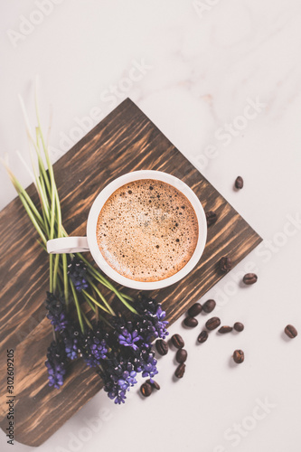 Cup of fresh americano or espresso coffee with golden foam froth on pile of brown raw coffee beans on white marble table background. Morning hot drink  coffee break  cope space