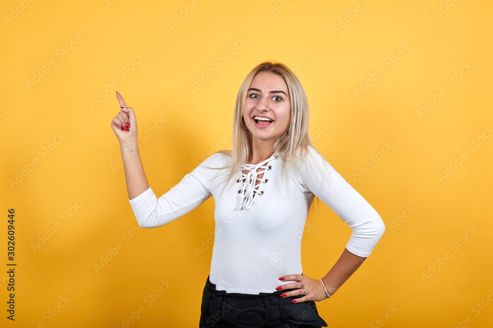 Obraz premium Beautiful caucasian young funny woman wearing pretty white shirt on isolated orange background looking smiling and keeping finger up
