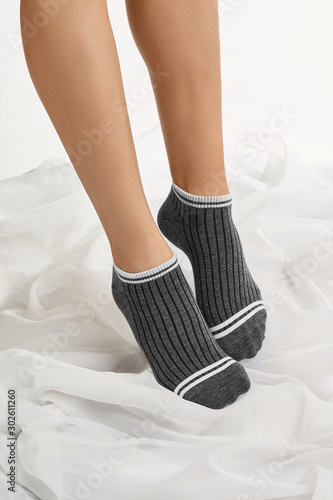 Cropped shot of a girl's feet, staying on a floor. There are short dark grey socks with white stripes on her feet. The photo was taken on a white background. 