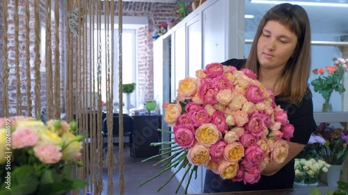 Portrait of professional florist woman making bouquet of pink and orange peonies in flower shop. Floral business concept. She creates professional bunch composition in floristic studio store.