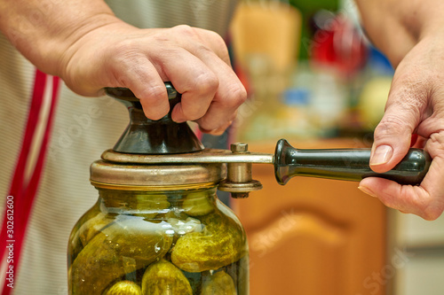 Preservation of fresh house cucumbers in glass jars using seamer. Closeup, selective focus