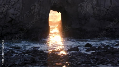 Sunlight streams through a keyhole arched rock at Pfeiffer beach at Big Sur located on the Pacific Ocean on the coast of California at sunset. 