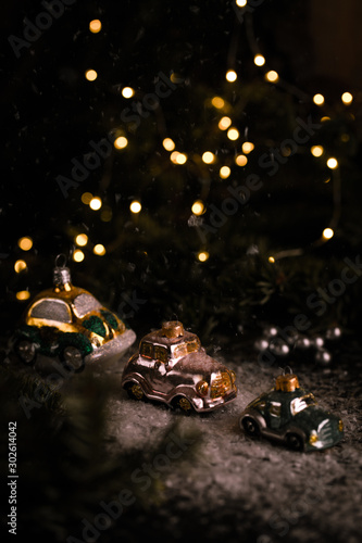 Christmas tree ornaments, tiny car on snowy table under the fir tree and bokeh lights with white candle in the background. Beautiful mysterious village decoration, greeting card, new year celebration 