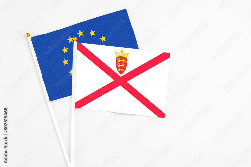 Jersey and European Union stick flags on white background. High quality fabric, miniature national flag. Peaceful global concept.White floor for copy space. Jersey and European Union stick flags on white background. High quality fabric, miniature national flag. Peaceful global concept.White floor for copy space.