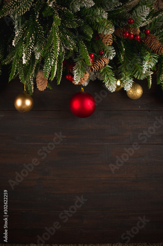 Christmas frame background with fir tree green branches, greeting card with decoration in red and golden colors on dark brown wooden board, copy space for text