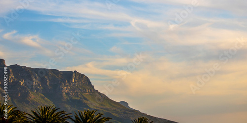 Golden blue cloudy sunset or sunrise over a mountain in Camps Bay, Cape Town and palm trees in the background.