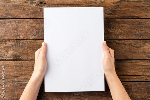 Overhead shot of woman’s hands holding blank paper sheet on rustic wooden table. Close up photo