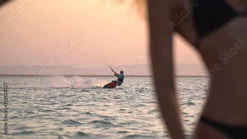 Kite surfer is gliding in the sea, blurred young women on the foreground