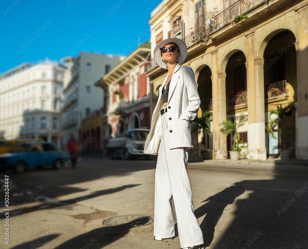 Stylish woman in a white suit and white hat on a city street. Cuba