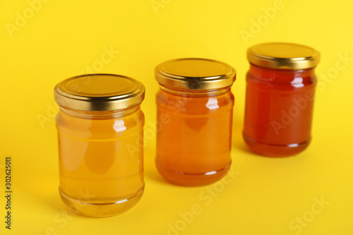 Jars with different types of organic honey on yellow background