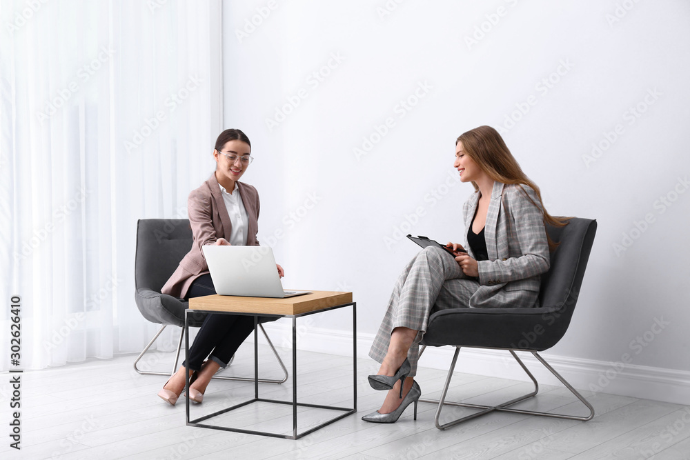 Young businesswomen sitting in armchairs at table indoors Young businesswomen sitting in armchairs at table indoors