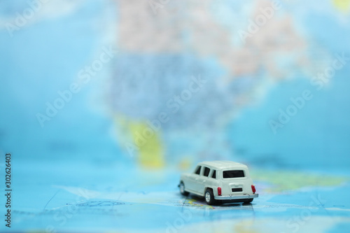 Closeup of miniature white car toy on colorful world map with copy space. Using for global travel and planning concept.