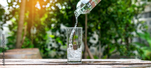 Drink water pouring in to glass over sunlight and natural green background.Select focus blurred background.