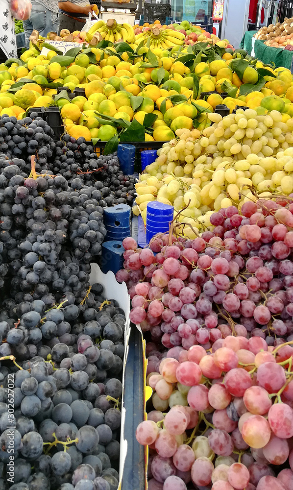 A trading place in the Turkish market, a counter filled with fresh fruits and vegetables: green, red and black grapes, fresh Turkish oranges with leaves, bananas A trading place in the Turkish market, a counter filled with fresh fruits and vegetables: green, red and black grapes, fresh Turkish oranges with leaves, bananas