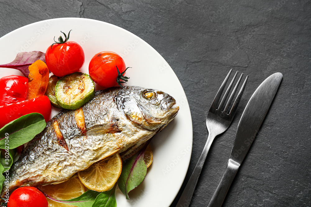 Delicious roasted fish with lemon and vegetables on dark grey table, flat lay Delicious roasted fish with lemon and vegetables on dark grey table, flat lay