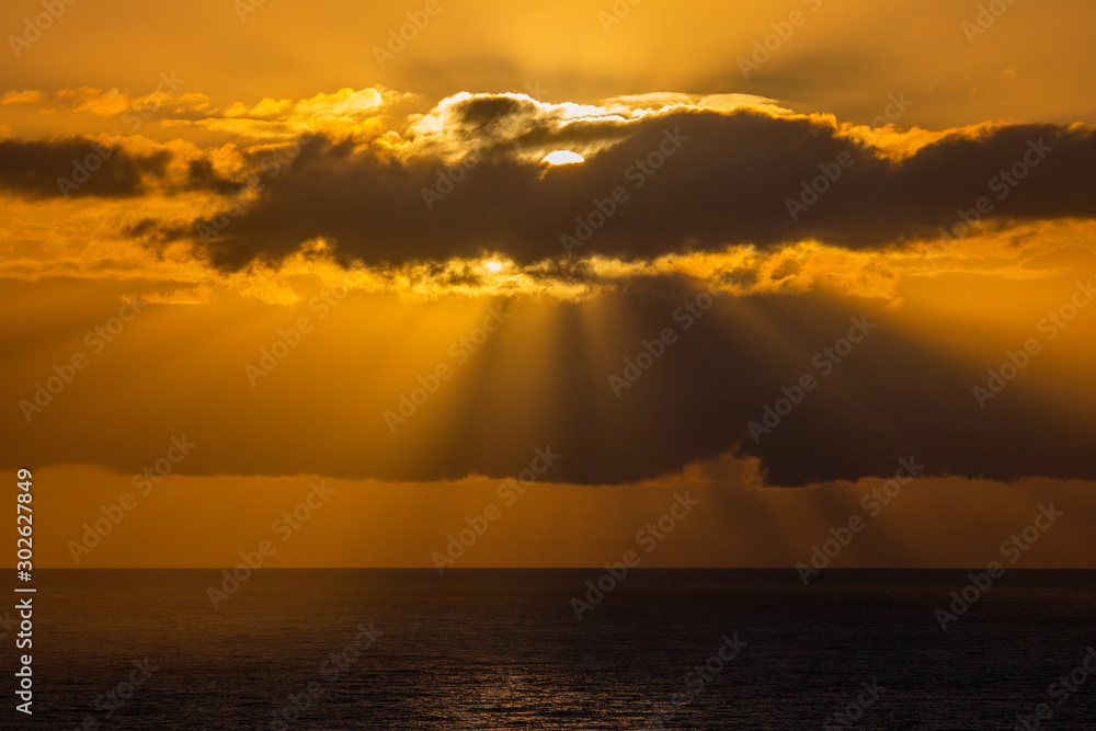 Dramatic golden sunset or sunrise over the ocean with God fingers through clouds.