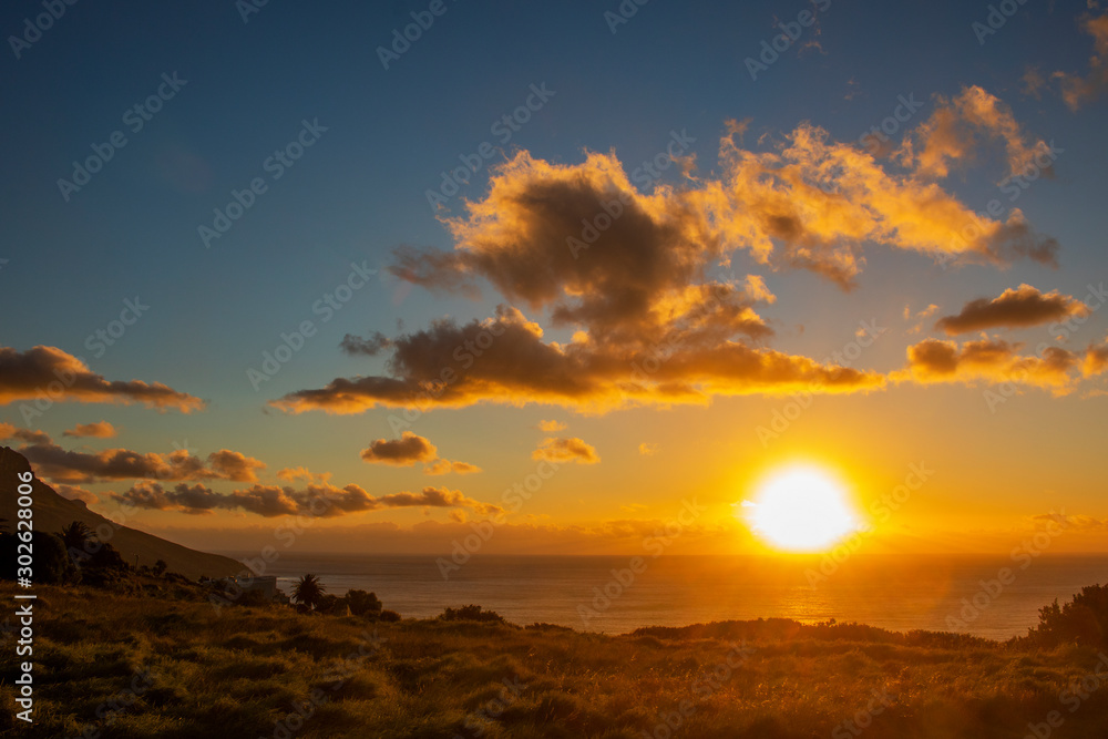 Fototapeta premium Grass meadow field at sunset or sunrise over the ocean in Camps Bay, Cape Town.