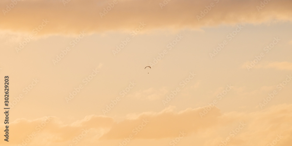 Paraglider floating through golden blue sunset or sunrise sky over Camps Bay, Cape Town.