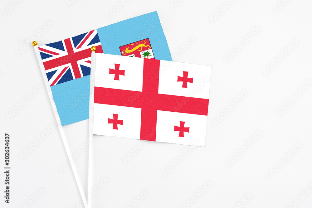 Georgia and Fiji stick flags on white background. High quality fabric, miniature national flag. Peaceful global concept.White floor for copy space.