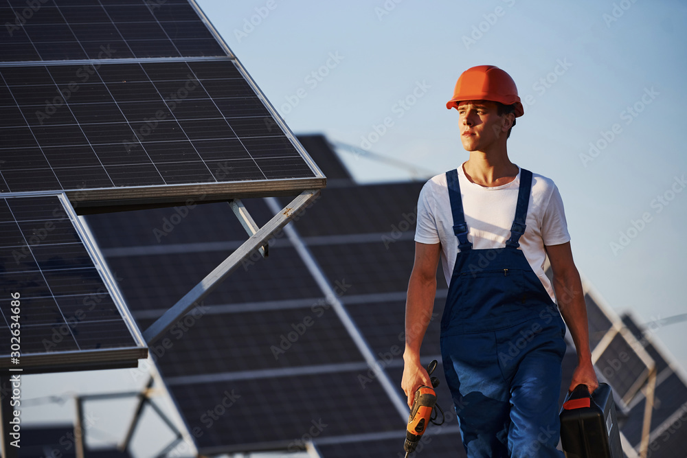 Cordless screwdriver in hand. Male worker in blue uniform outdoors with solar batteries at sunny day Cordless screwdriver in hand. Male worker in blue uniform outdoors with solar batteries at sunny day