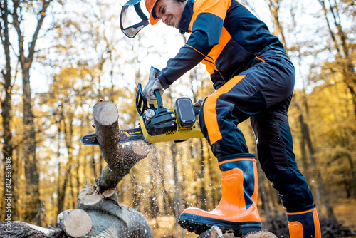 Professional lumberjack in protective workwear working with a chainsaw in the forest, sawing a thick wooden log