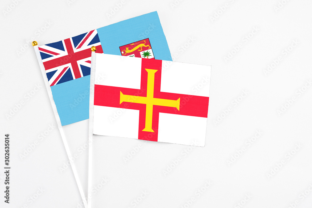 Guernsey and Fiji stick flags on white background. High quality fabric, miniature national flag. Peaceful global concept.White floor for copy space.