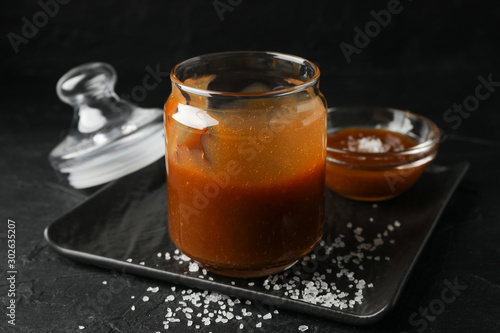 Glass jars with salted caramel on black background, close up