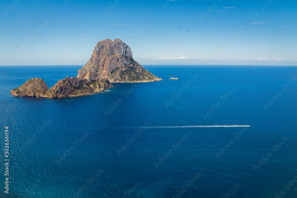 View of the famous mysterious island Es Vedrà from the famous view point on the cliffs above beach Cala D'Hort beautiful island of Ibiza, Spain, scenic blue sea, horizon sky  
