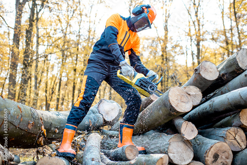 Professional lumberjack in protective workwear working with a chainsaw in the forest, sawing wooden logs