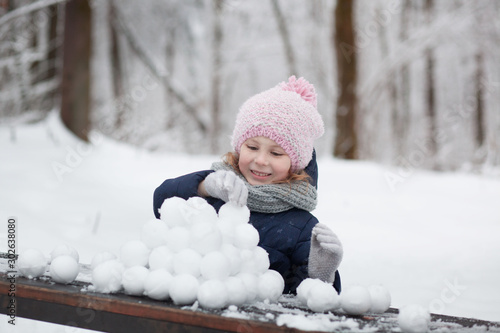 happy child girl playing with snow on snowy winter walk, making snowballs in the park