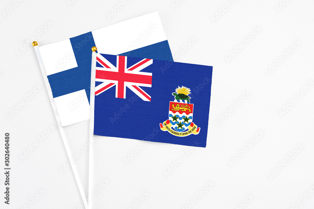 Fototapeta premium Cayman Islands and Finland stick flags on white background. High quality fabric, miniature national flag. Peaceful global concept.White floor for copy space.