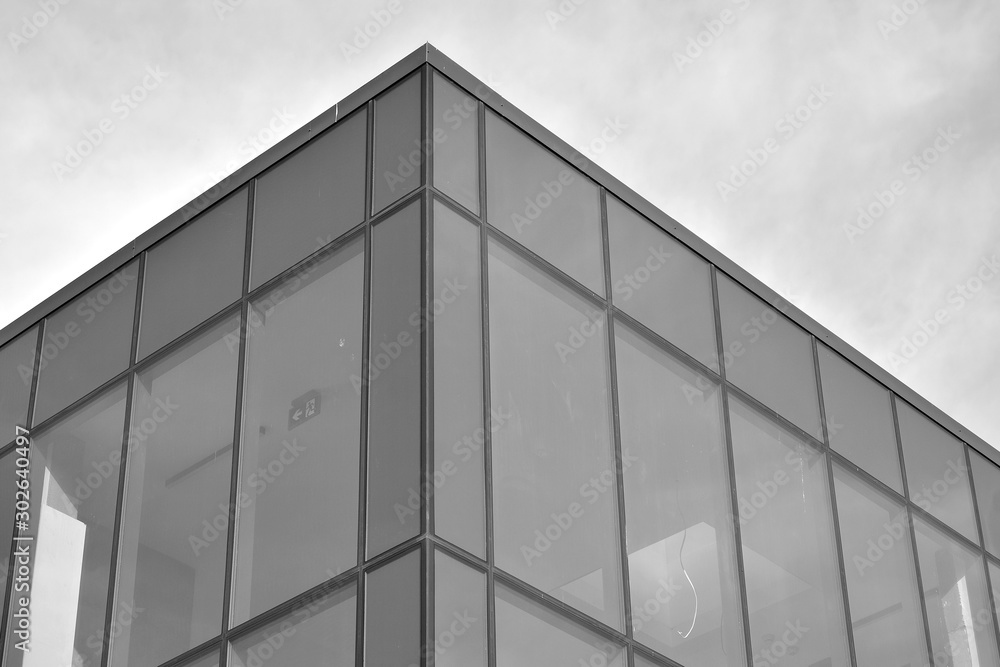 Curtain wall made of toned glass and steel constructions under sky. A fragment of a building. Black and white. Curtain wall made of toned glass and steel constructions under sky. A fragment of a building. Black and white.