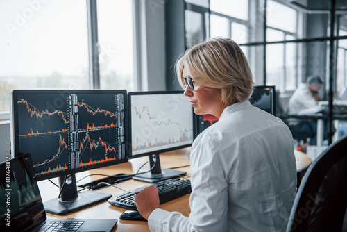 Fotografie Female stockbroker in formal clothes works in the office with financial market
