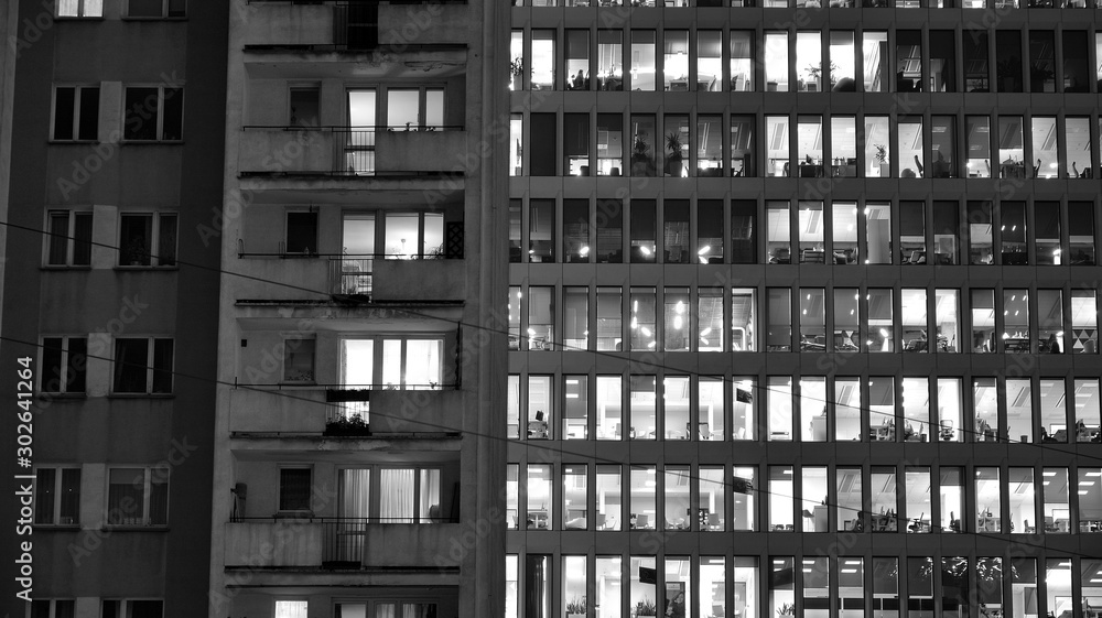 Obraz premium Pattern of office buildings windows illuminated at night. Lighting with Glass architecture facade design with reflection in urban city. Black and white.