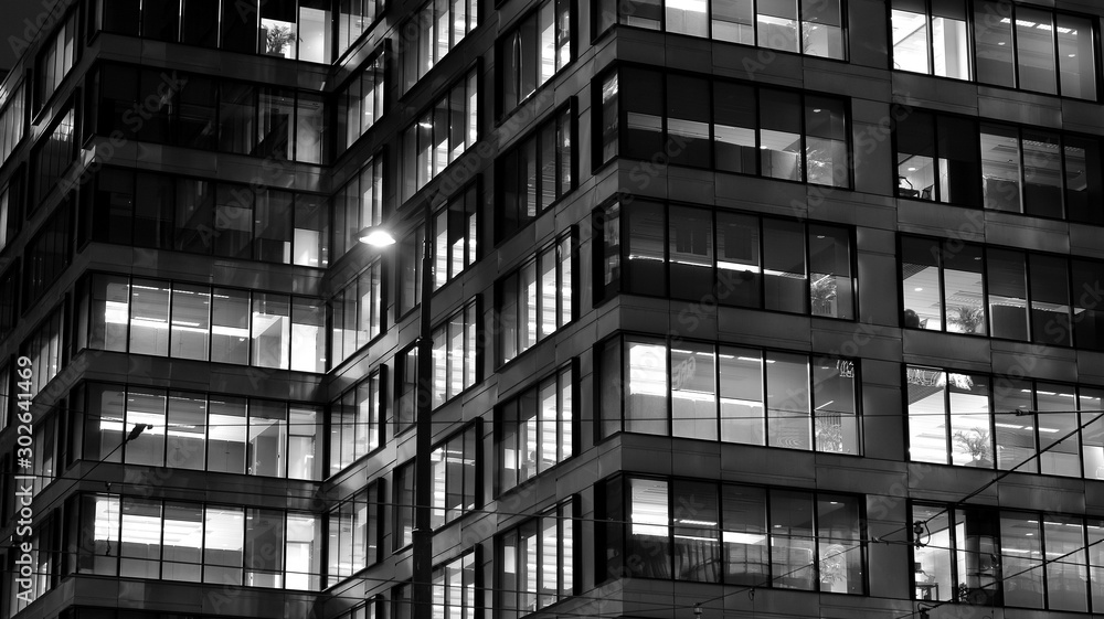 Obraz premium Pattern of office buildings windows illuminated at night. Lighting with Glass architecture facade design with reflection in urban city. Black and white.