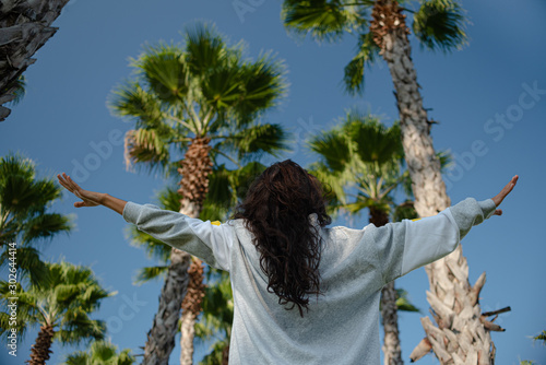 brunette girl long hair back hands raised to the sky tops of palm trees