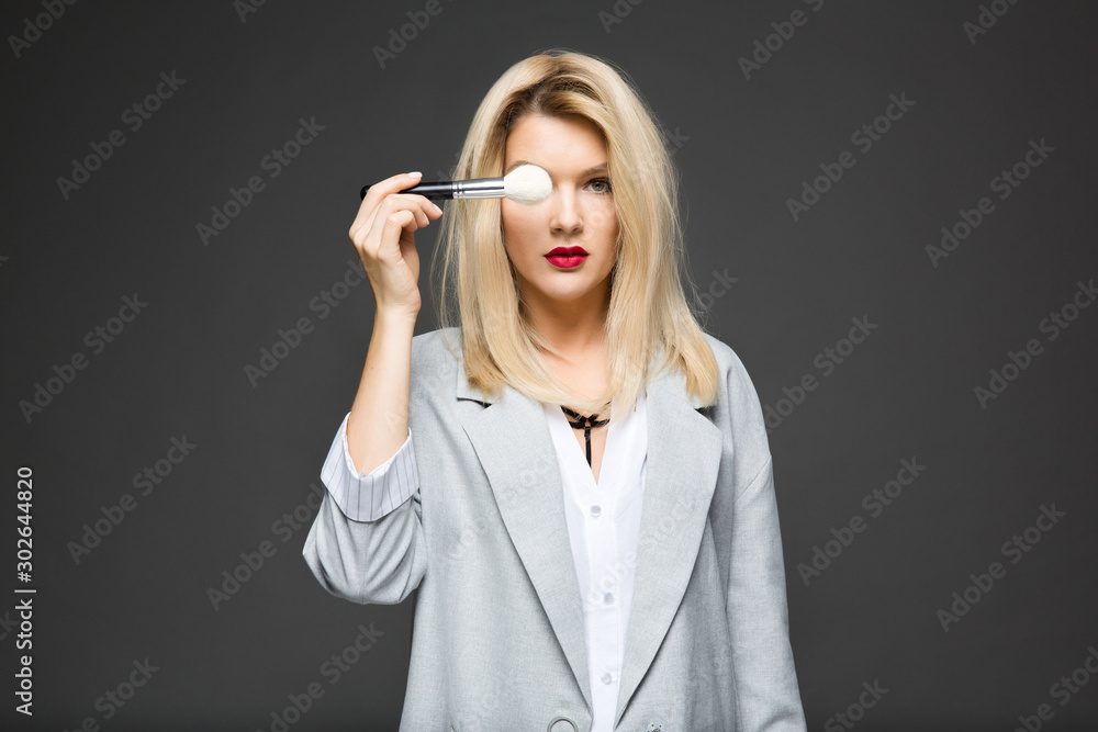 girl makeup artist in a blouse and a jacket holds makeup brushes in her hand, isolated on gray background girl makeup artist in a blouse and a jacket holds makeup brushes in her hand, isolated on gray background