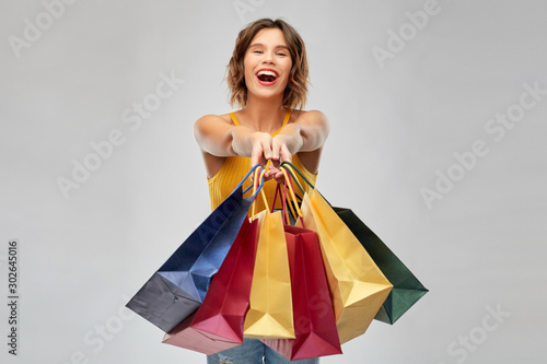 sale and people concept - happy smiling young woman in mustard yellow top and jeans with shopping bags over grey background