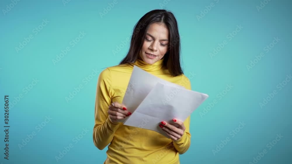 Serious businesswoman standing on blue background. She is satisfied with work of staff. Pretty hispanic female boss checks documents, utility bills. Serious businesswoman standing on blue background. She is satisfied with work of staff. Pretty hispanic female boss checks documents, utility bills.