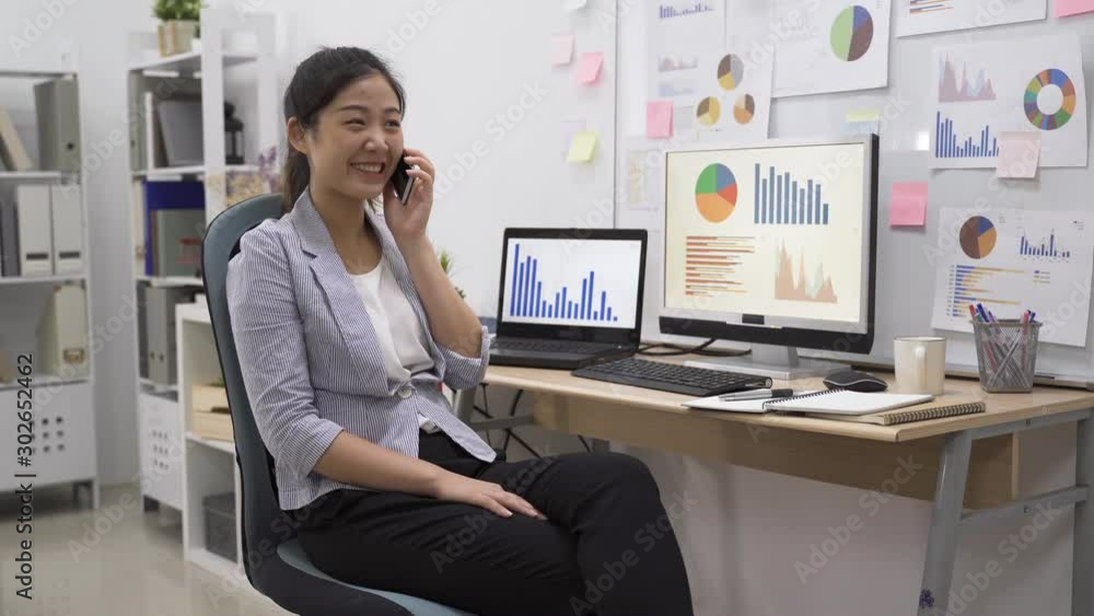 Smiling young businesswoman talking on mobile phone while working at office. relax asian korean lady employee chatting on cellphone and joyful laughing with friend. female worker enjoy conversation Smiling young businesswoman talking on mobile phone while working at office. relax asian korean lady employee chatting on cellphone and joyful laughing with friend. female worker enjoy conversation