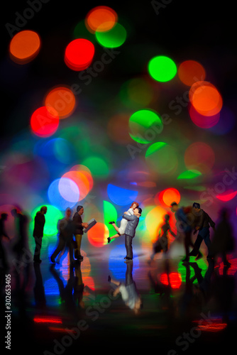 Fototapeta Naklejka Na Ścianę i Meble -  Miniature toy -A couple hugging together among busy commuters crowd with colorful bokeh lights, happiness concept.
