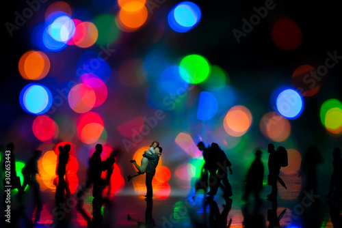 Miniature toy -A couple hugging together among busy commuters crowd with colorful bokeh lights, happiness concept.