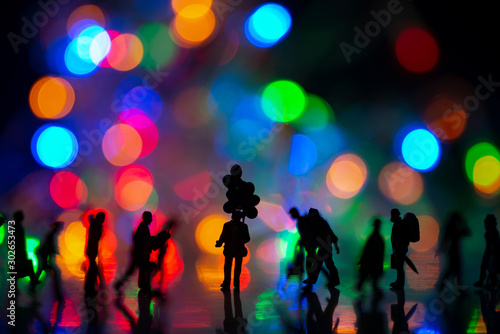 Miniature toy - Silhouette of a man holds colorful balloons among busy commuters crowd with colorful bokeh lights, waiting for someone concept.