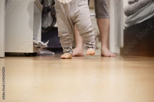 baby walking away from mother. small kid walk on bedroom wooden floor. mother sitting in wait. warm loving family concepts. happy moments of children growing up. © suebsiri