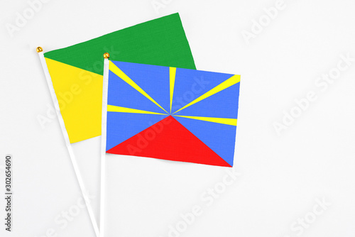 Reunion and French Guiana stick flags on white background. High quality fabric, miniature national flag. Peaceful global concept.White floor for copy space.