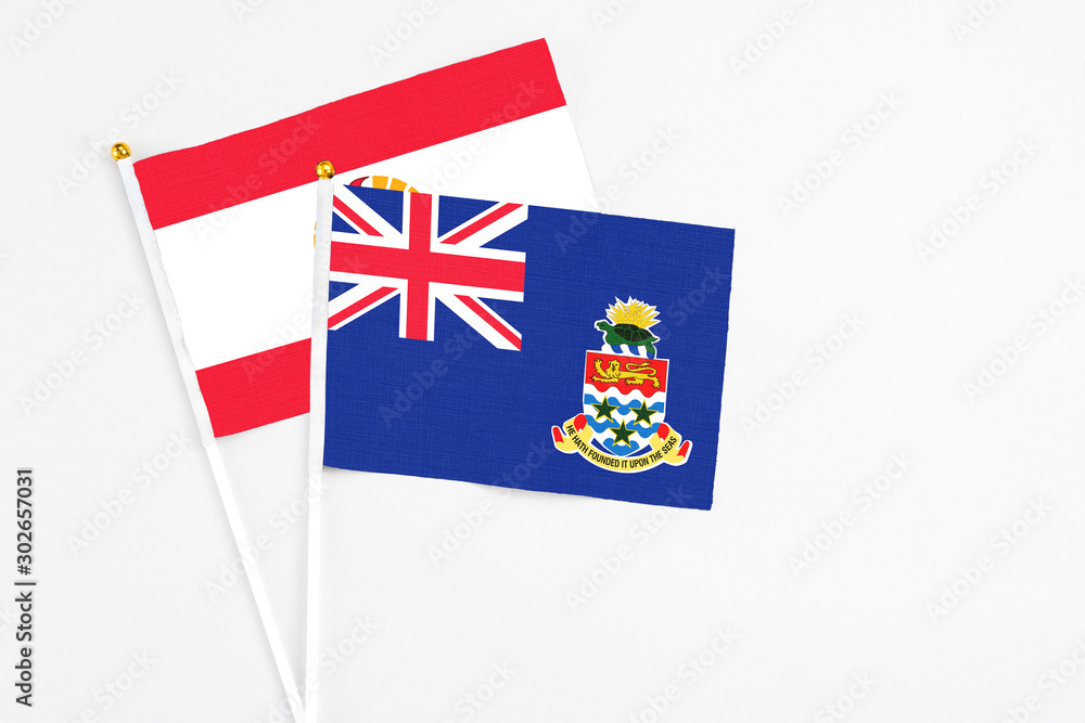 Fototapeta premium Cayman Islands and French Polynesia stick flags on white background. High quality fabric, miniature national flag. Peaceful global concept.White floor for copy space.