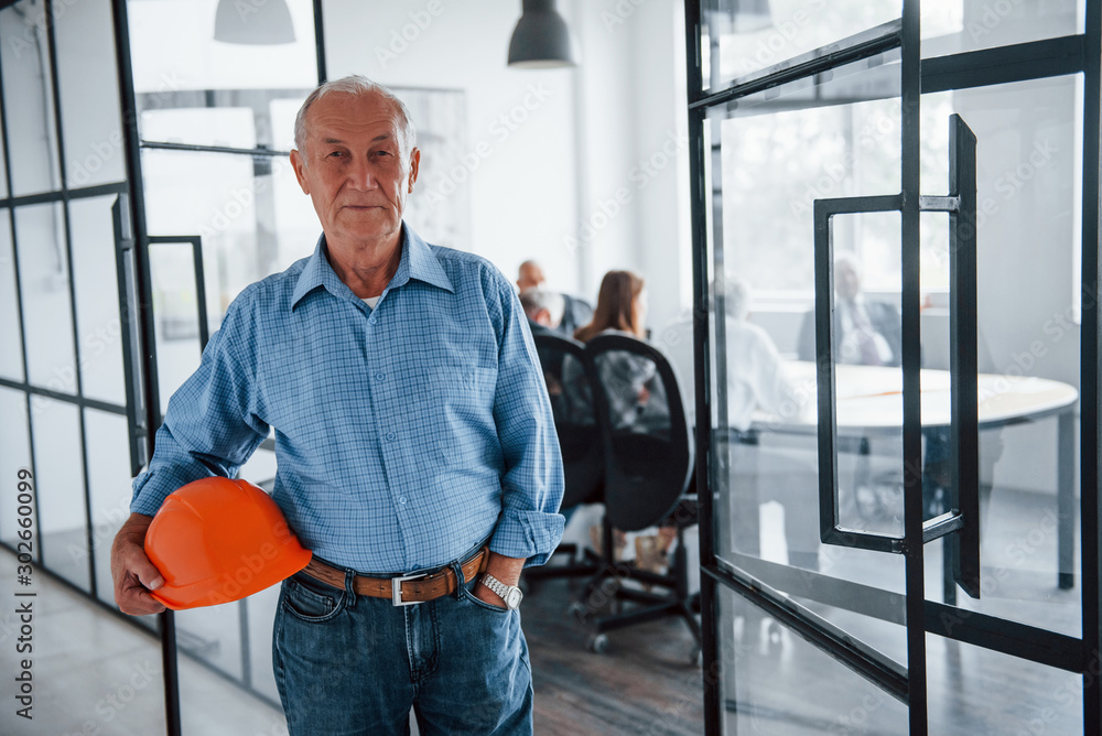 Portrait of senior man that stands in front of aged team of elderly businessman architects that have a meeting in the office Portrait of senior man that stands in front of aged team of elderly businessman architects that have a meeting in the office