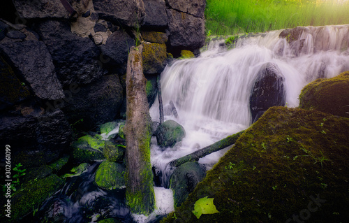 Fototapeta Naklejka Na Ścianę i Meble -  Waterfall with boulders with moss in the foreground and a tree trunk lying in the water